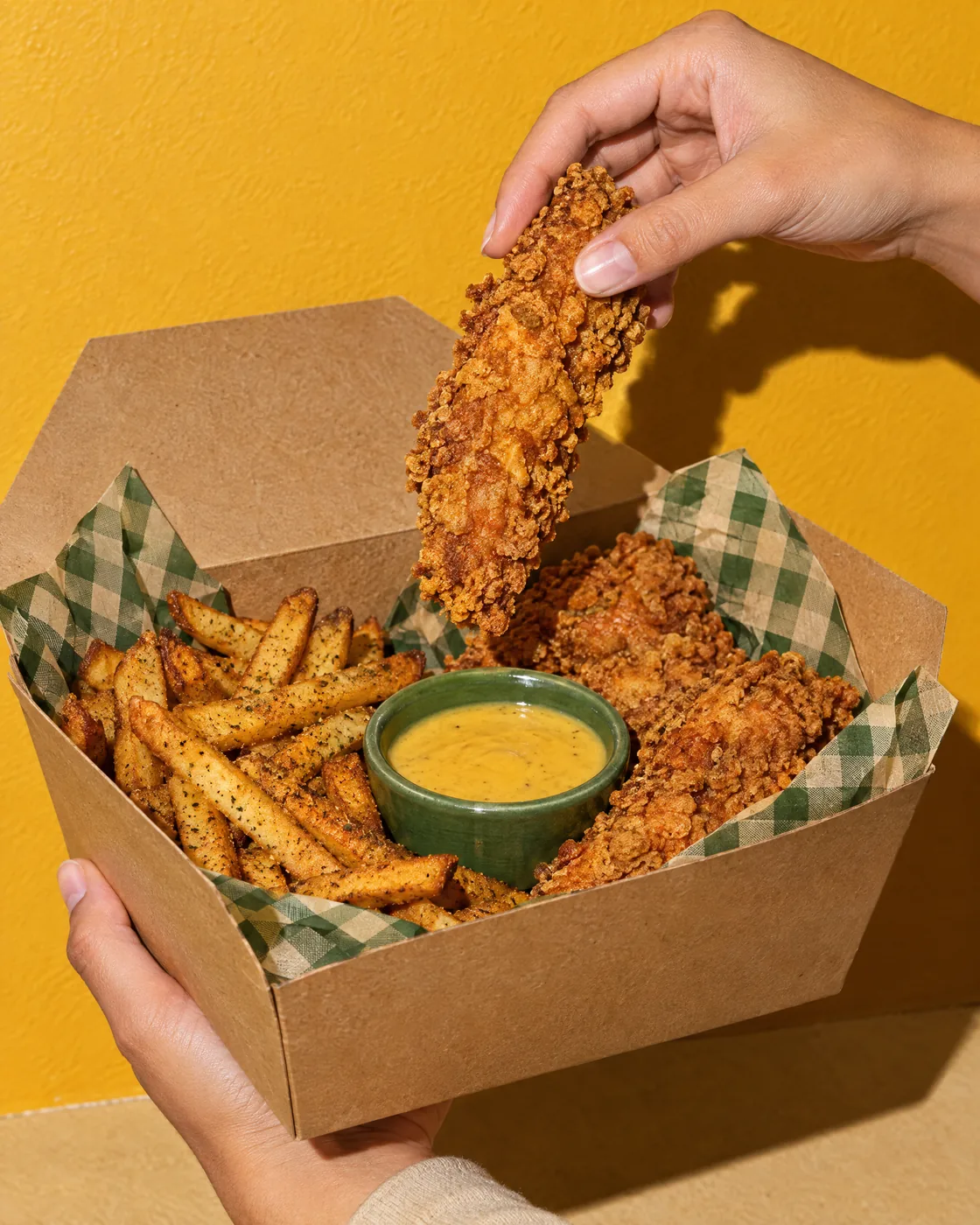 Hand lifting a crispy tender out of the box